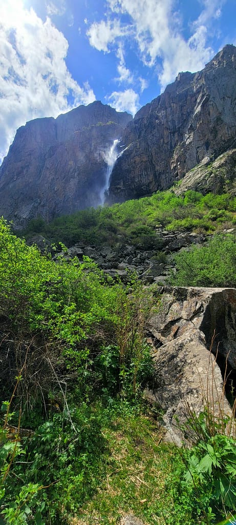 View of Belogorka Waterfall cascading down a steep cliff face surrounded by lush green shrubs and rocky terrain